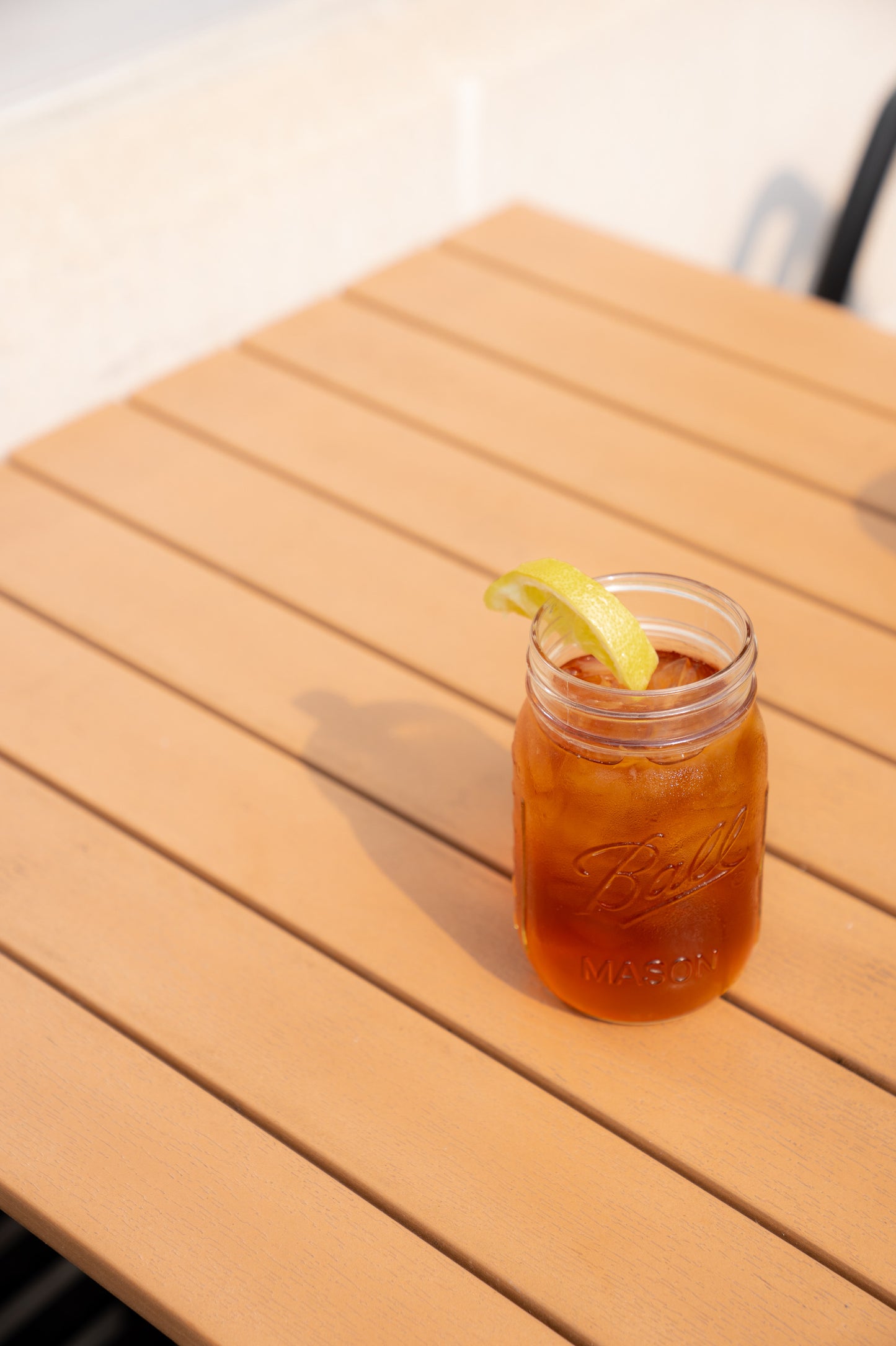 Mason jar filled with iced tea and a lemon wedge on a wooden table.