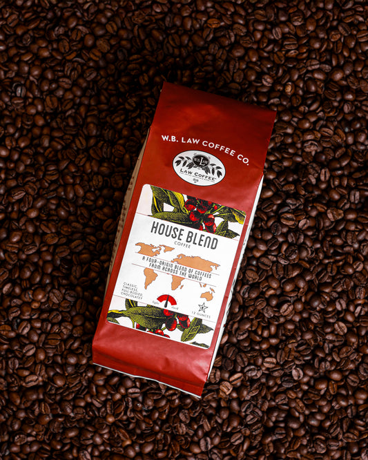 A 12oz bag of House Blend coffee beans from W.B. Law Coffee Co. placed on a background of whole coffee beans.