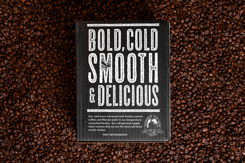 A ironbound cold brew coffee box reading Bold, Cold, Smooth & delicious sitting on a pile of coffee beans.