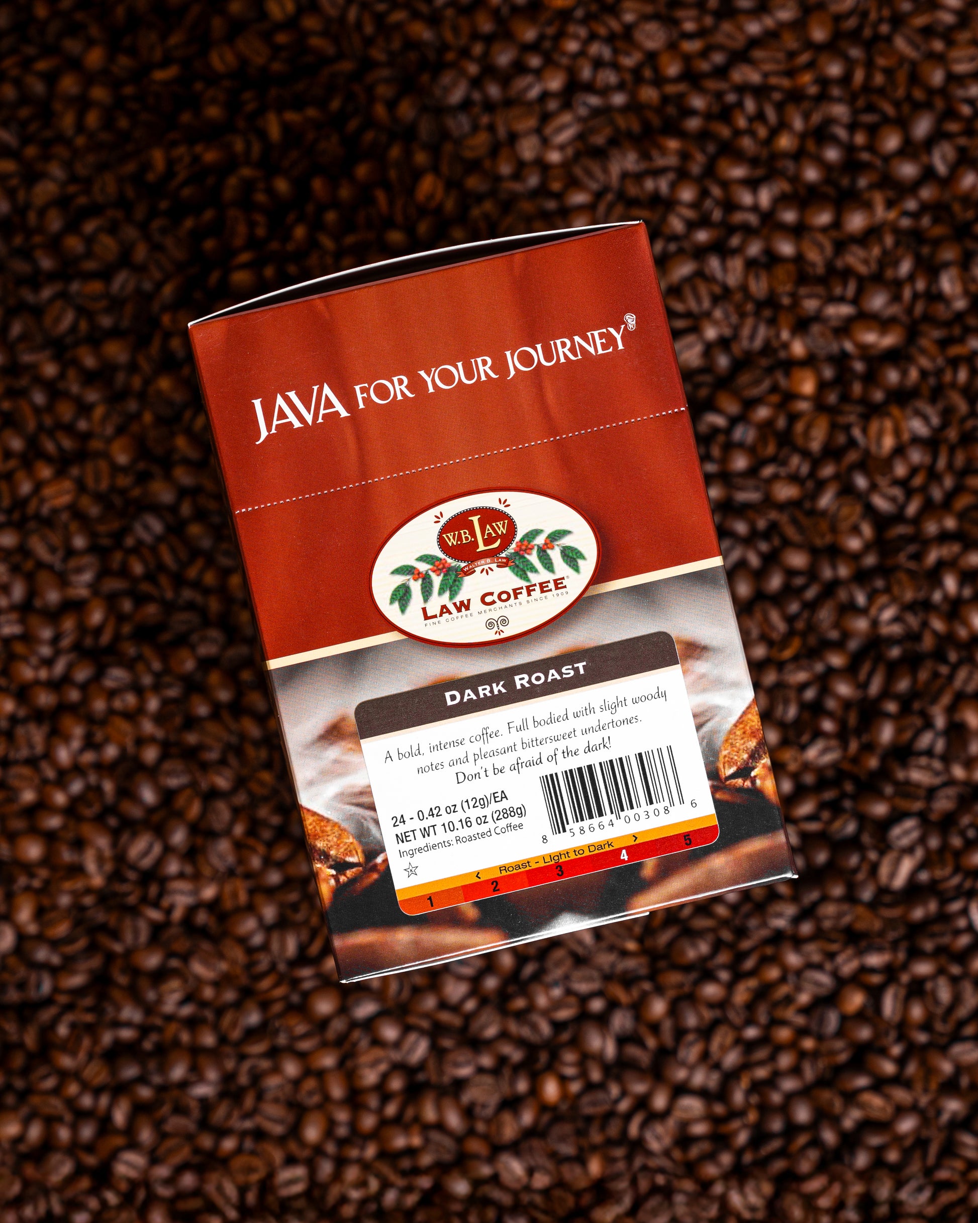 A pack of Dark Roast Coffee single serve cups lying on a bed of coffee beans, with the product branding visible on the packaging.