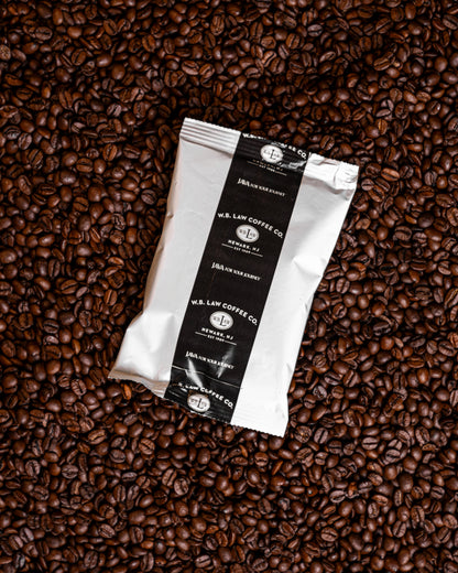 A black and white 2.5oz frac pack of WB Law Coffee dark roast ground coffee on a bed of coffee beans