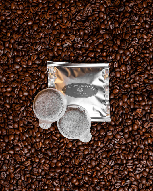 Two double decaf espresso pods sitting on its packaging on a bed of coffee beans. 