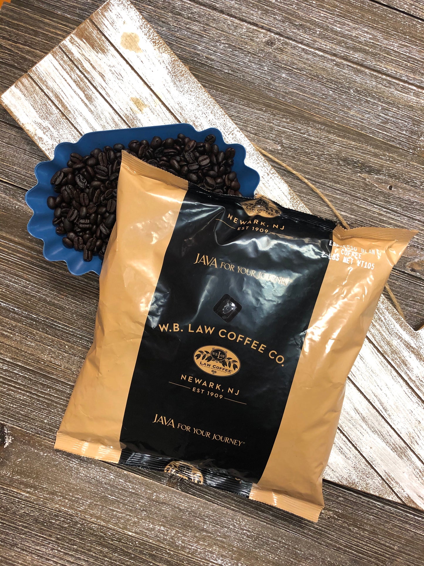 A 2lb bag of cafe mendez espresso bean sitting on some coffee beans and a wood table.